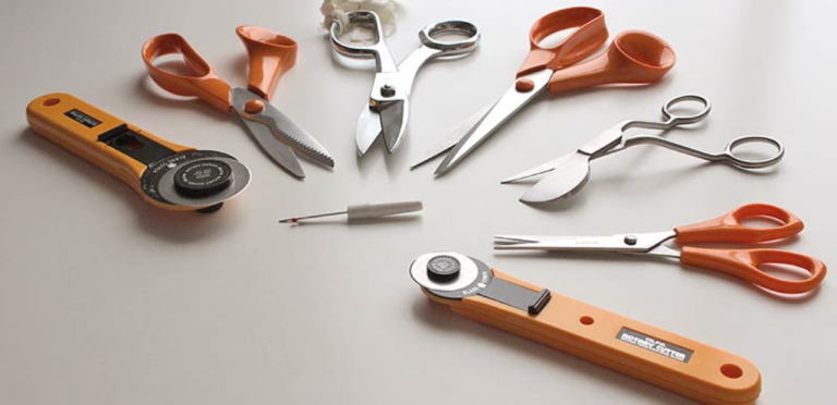 best fabric cutting tools collection showing scissors rotary cutter and electric fabric cutter on cutting mat