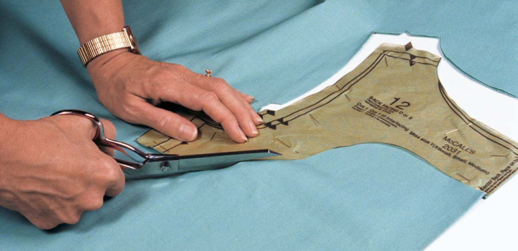A tailor manually cutting fabric with scissors ideal situations where hand cutting makes more sense than machine cutting