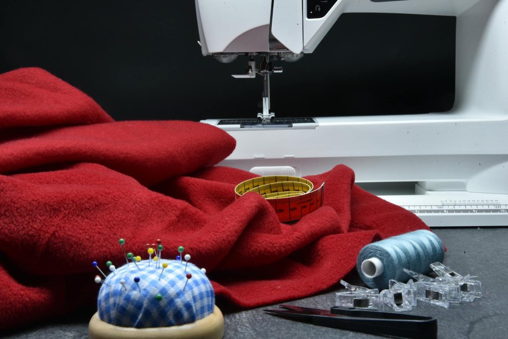 Close-up of a sewing setup with red fabric, sewing machine, thread, and measuring tape.